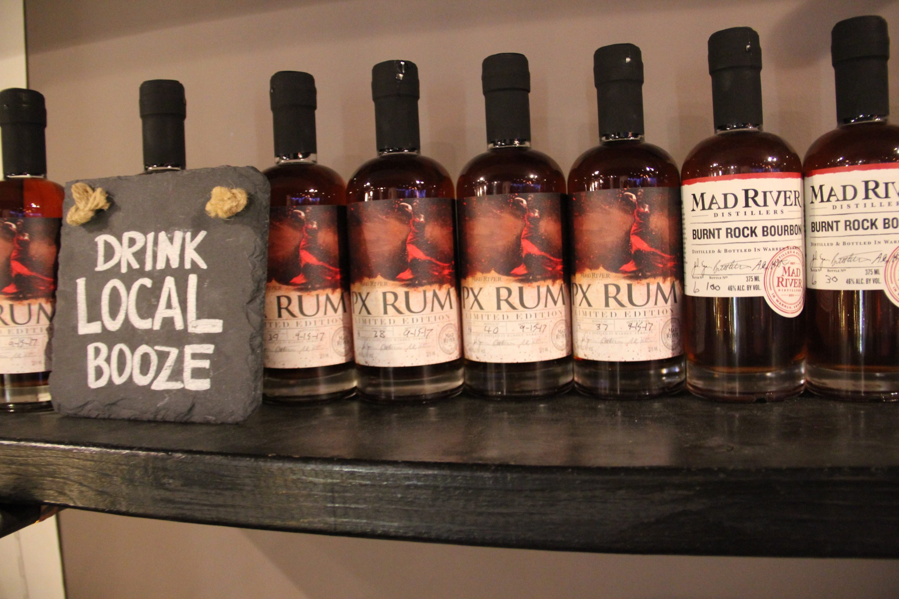 Mad River Distillers rum line up with a sign that says "drink local booze"