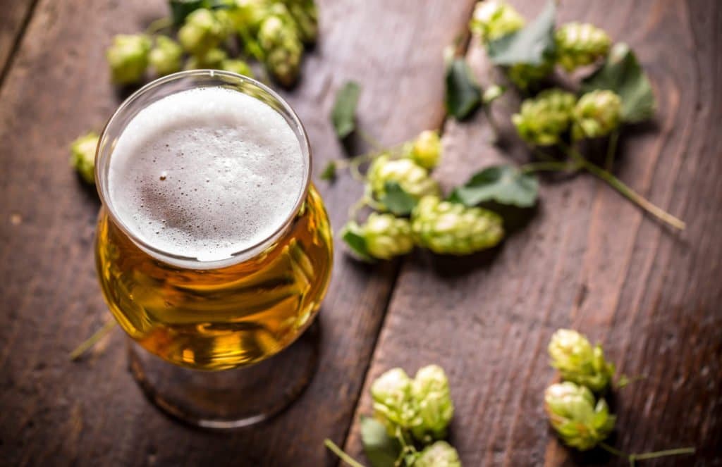 IPA in a glass on vintage wooden surface with hops strewn around