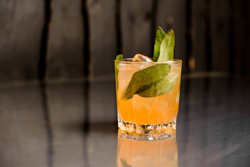 Glass of cider on a dark background with sage leaves in it