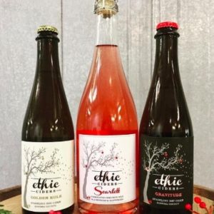 Three Bottles of Ethic Cider that are part of the holiday box on a barrel against a light background
