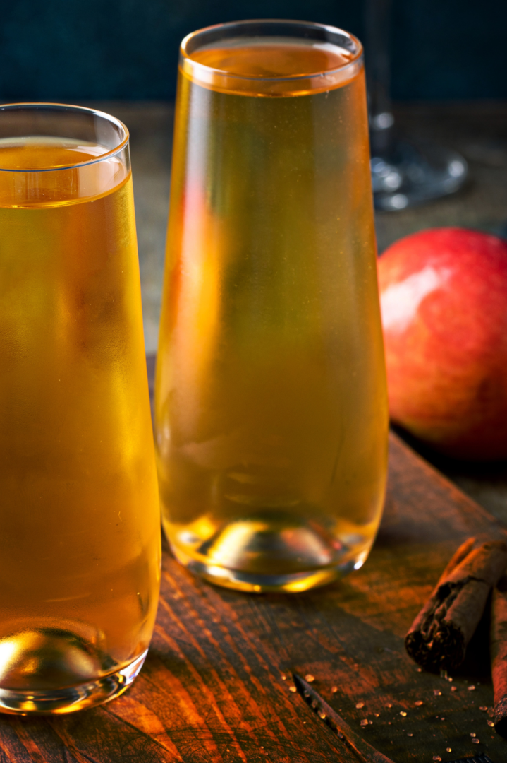 Cider Cocktails with Apple Landscape cider cocktails on a cutting board with apples and cinnamon sticks